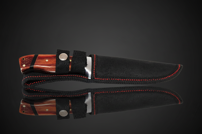 Couteau à lame fixe avec manche en bois naturel brun-rouge inséré dans sa gaine en Cordura noire avec couture rouge et clip de ceinture – fond sombre avec effet miroir